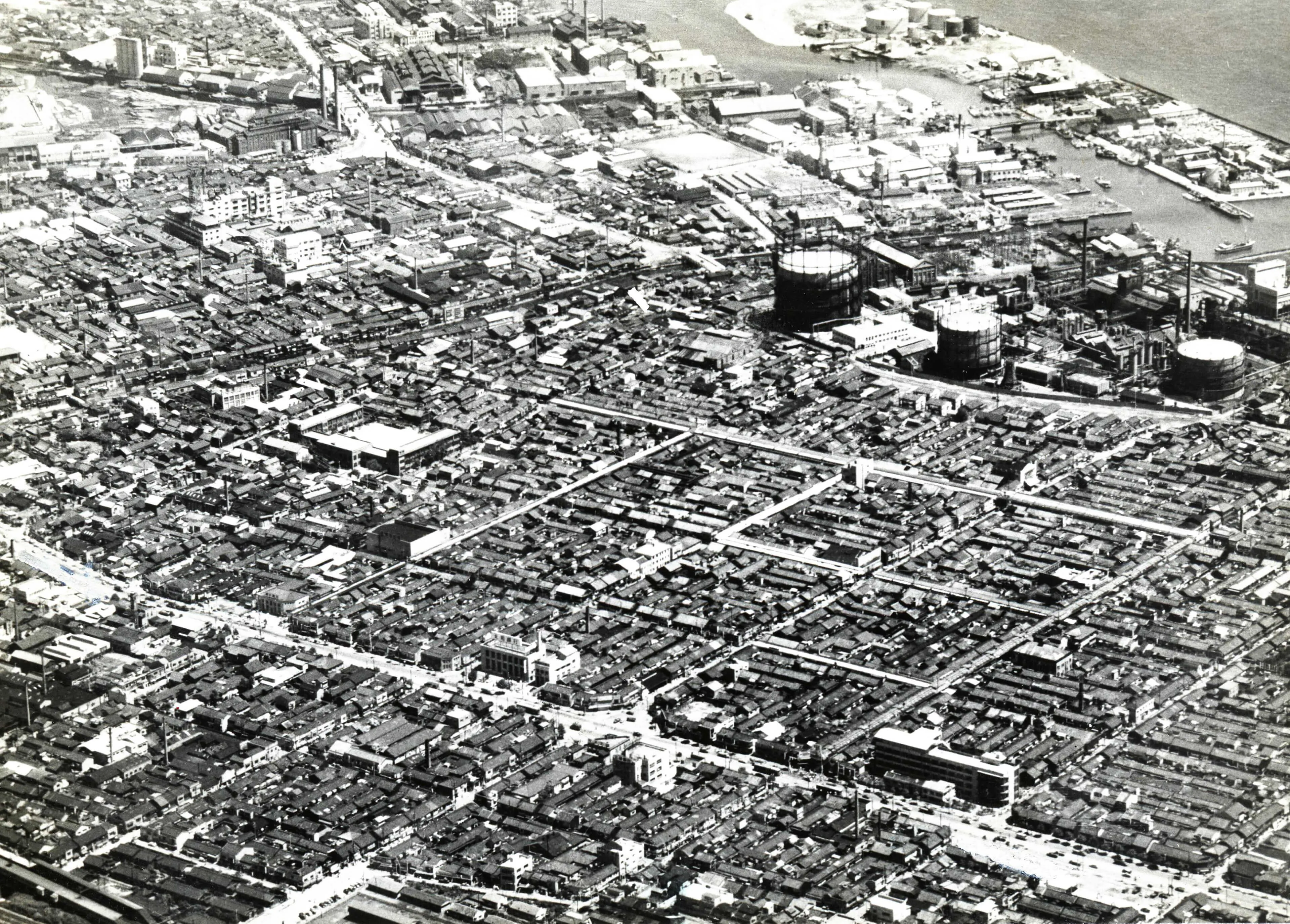 空撮写真。街と遠くに大きな建造物あり。下に写真の説明あり。